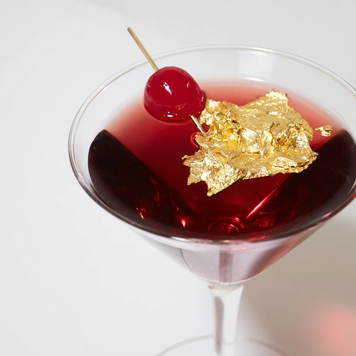 Opulent close-up of a Rococo Cherry Martini, showcasing gold flakes and a vibrant cocktail cherry.