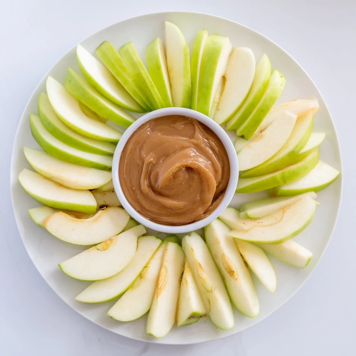 A close-up of a shareable platter of apple slices with rich, homemade caramel dip.