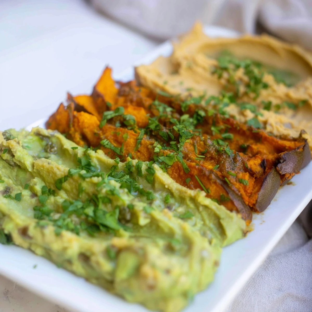 A vibrant dip trio: creamy avocado, red pepper, and turmeric hummus displayed beautifully.