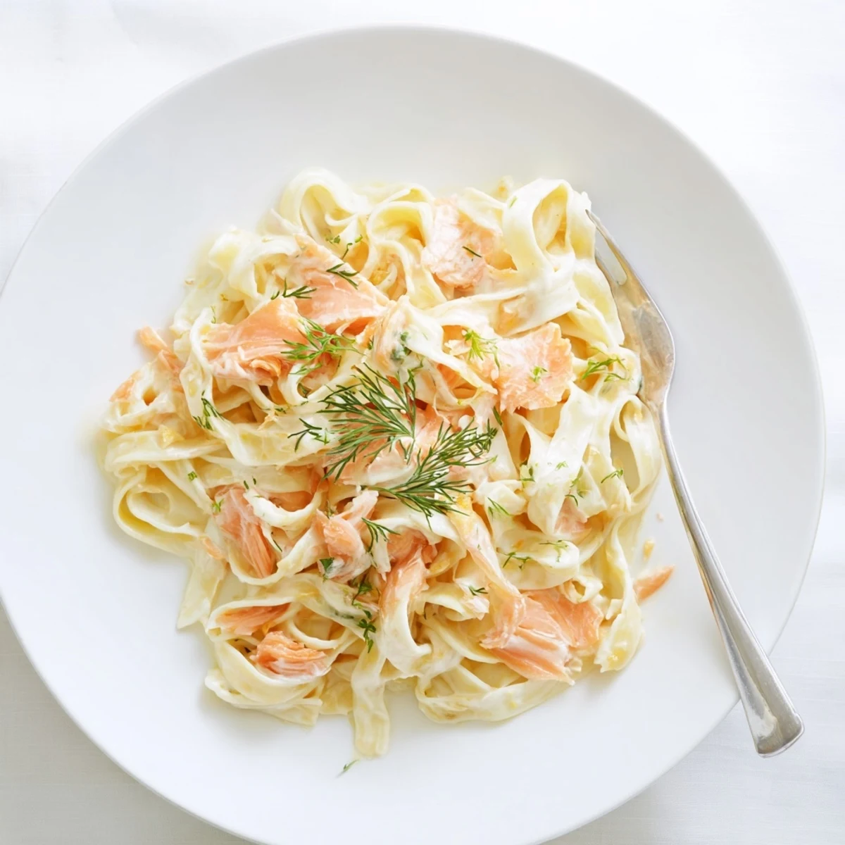 Fettuccine al horno con salmón ahumado en salsa cremosa, espolvoreado con eneldo fresco y limón.
