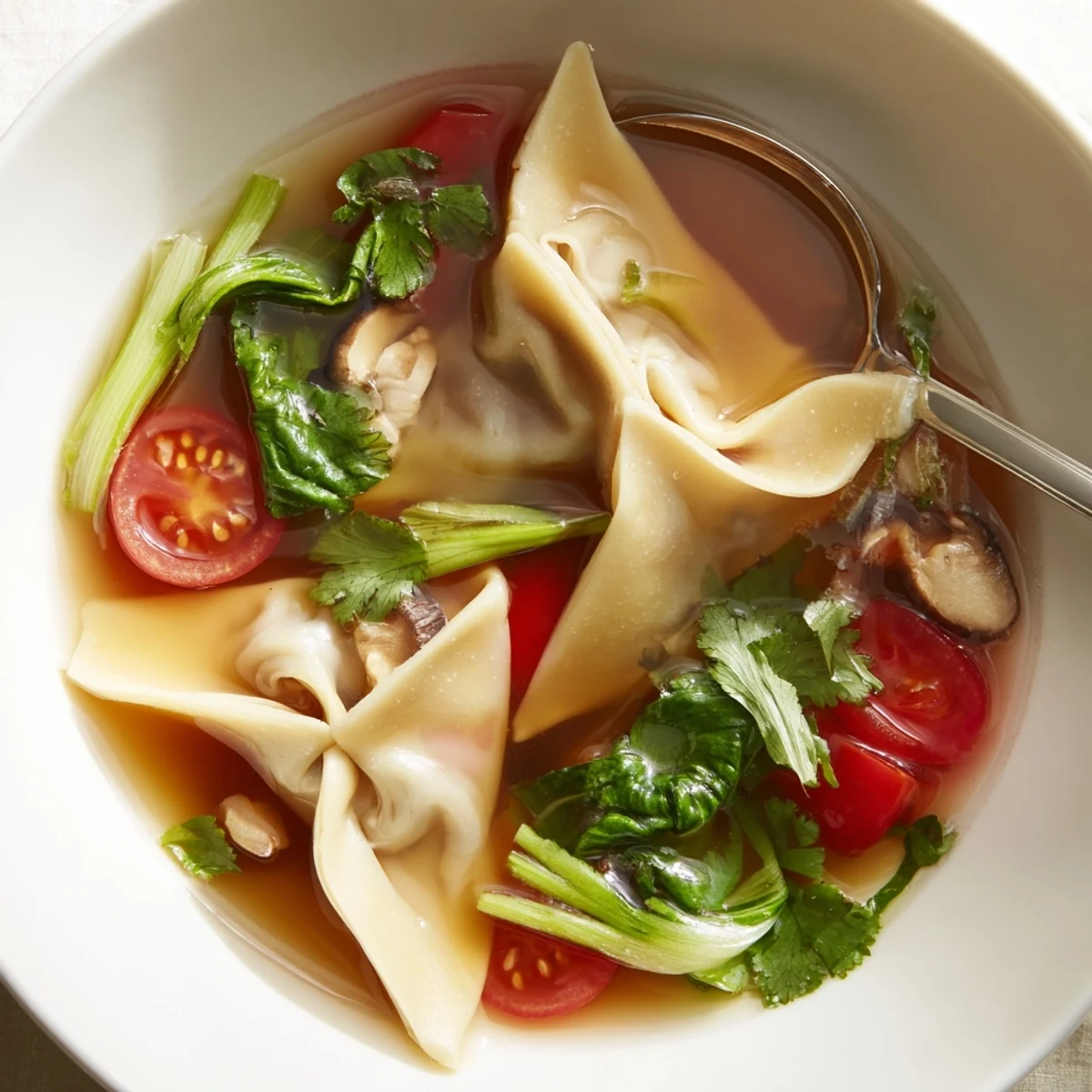 A close-up bowl of steaming Tom Yum Wonton Soup, featuring plump pork dumplings and vibrant lime broth.