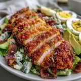 Cobb salad with Parmesan Crusted Chicken thighs, creamy avocado, and crispy bacon on a bed of fresh greens.