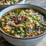 Caldo reconfortante de Egg Roll Soup con pollo y col en tazón, con zanahorias y cebolín, servido con cucharada de chili crisp picante.