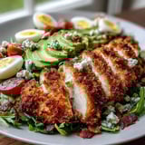 Sliced Parmesan Crusted Chicken tops vibrant greens, blue cheese, and eggs in this hearty salad.