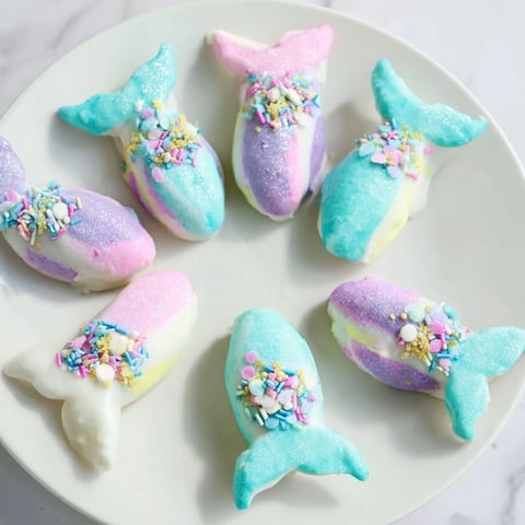 Delicate Mignardises Queue de Sirène, pastel madeleines shaped like mermaid tails, dipped in white chocolate and sprinkles.