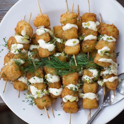 Golden-brown Patatas Pops drizzled with tangy pickle aioli, perfect for gatherings.  
