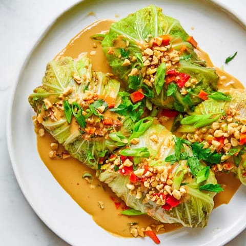 Steaming savoy cabbage rolls served with rich Thai peanut sauce and chopped peanuts, ready to eat.