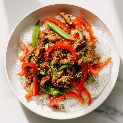 A close-up of a steaming bowl of Mongolian Chicken with Rice Noodles, savory and delicious.