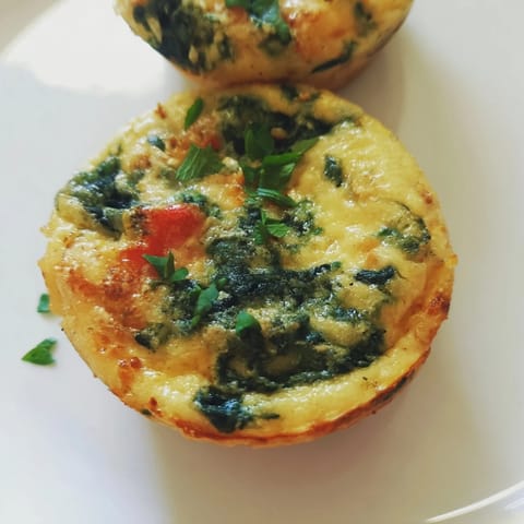 A close-up of savory Mini Crustless Quiches, ready to eat, highlighting the eggs and herbs.