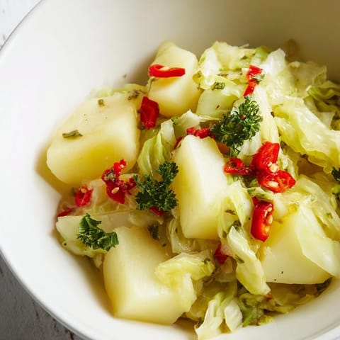 Repollo braisé con papas y chiles servido caliente con perejil y limón, un plato vegetariano apto para cenas acogedoras.