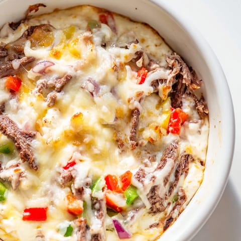 Creamy Philly Cheesesteak Dip in a ceramic bowl, featuring tender ribeye, sautéed peppers and onions with a side of crostini.  