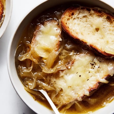French Onion Soup humeante en cuenco, con trozos de baguette y hierbas frescas.