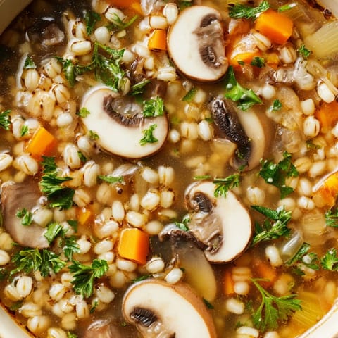 Un primer plano de la sopa de cebada con champiñones, destacando las rodajas de champiñones blancos y la cebada tierna.