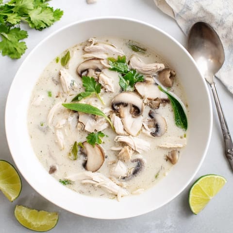 Tom Kha servido caliente, con un chorrito de lima y rodajas de pollo sobre un fondo marrón.