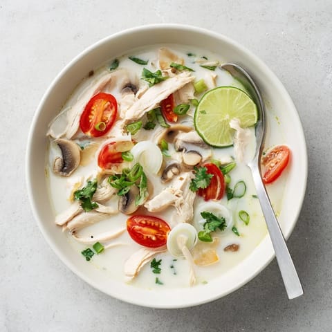 Una tazón de la sopa Best Ever Tom Kha Gai servida con rodajas de limón y cilantro.