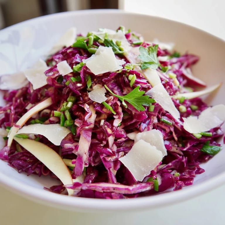 Ensalada crujiente de col lombarda con manzana y parmesano, servida en una mesa con aderezo en vinaigrette.